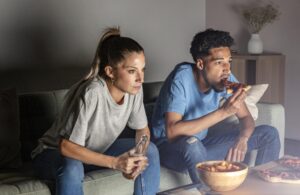 Homem E Mulher Tomando Cerveja E Lanches Em Casa Enquanto Assistem Tv